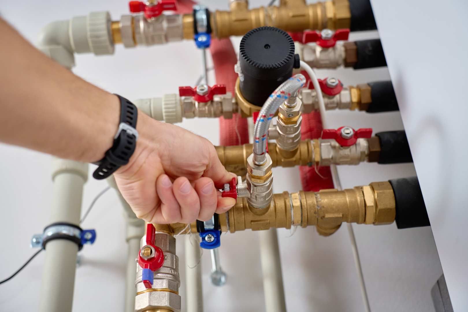 Close Up Of Technician Hand Adjusting Valve On Heat Pump Piping System With Pipes And Fittings.