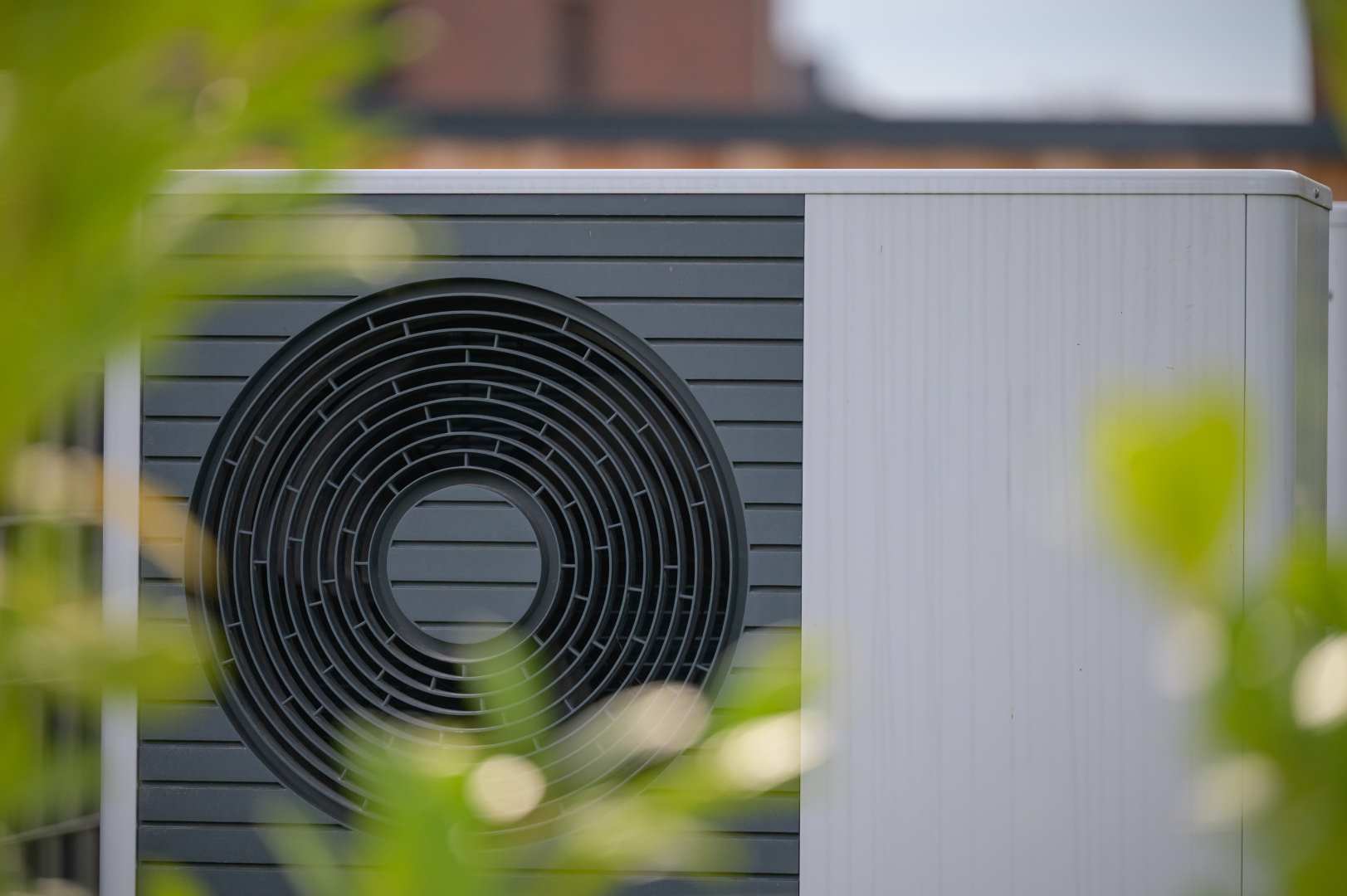 Close Up View Of Heat Pump Unit With A Circular Fan Design Framed By Soft Green Foliage